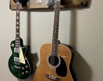 May include: Two guitars hanging on a wooden wall mount. The guitar on the left is green with a white pickguard and the guitar on the right is brown with a black pickguard.