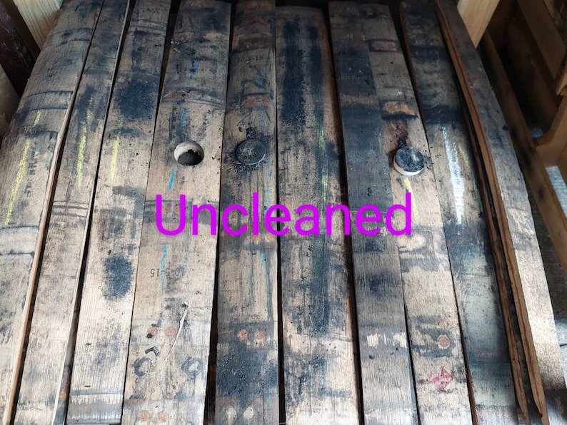 May include: Close-up of a wooden barrel stave, showing the natural wood grain and dark brown color. The stave has a circular hole and a black metal cap. The word "Uncleaned" is written in pink letters across the stave.