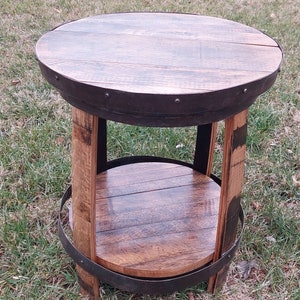 May include: A round wooden table with a metal band around the top and bottom. The table has a shelf in the middle and is made from reclaimed wood.