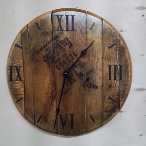 May include: A wooden clock with Roman numeral markings on a brown wooden background. The clock face has black hands and a black center. The clock face has a label that reads "DISTO 3BURD WHISK P KY 230 TANK 206 C04 C24 L-386".