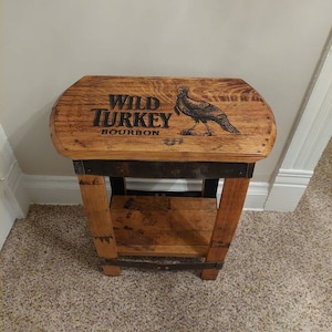 May include: A wooden stool with a shelf, made from a repurposed whiskey barrel. The top of the stool has a black and white image of a turkey with the words "Wild Turkey Bourbon" printed on it.