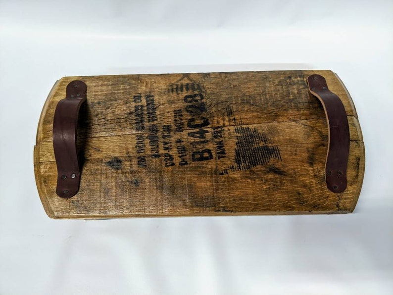 May include: A wooden serving tray made from a reclaimed whiskey barrel with two leather handles. The tray has a brown stain and the text "B&C 231" is printed on the surface.