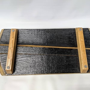 May include: A wooden serving tray made from reclaimed barrel staves. The tray has a black charred finish and is supported by two wooden legs attached with metal screws.