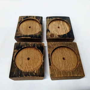 Könnte beinhalten: Vier quadratische Untersetzer aus Holz mit einer dunkelbraunen Beize und einem runden Ausschnitt in der Mitte. Die Untersetzer sind aus recyceltem Holz gefertigt.