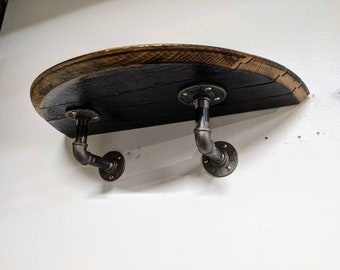 May include: A wooden shelf made from a reclaimed barrel stave, with black stain and a natural wood edge. The shelf is supported by two black metal pipe brackets.