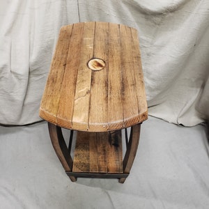 Pu&ograve; includere: Un tavolino in legno fatto a mano con doghe di botte riciclate. Il tavolo presenta un piano rettangolare con bordi arrotondati e un ripiano inferiore. Il legno ha un aspetto naturale e invecchiato con venature visibili e un colore marrone caldo. Il tavolo &egrave; sostenuto da gambe in legno curve.