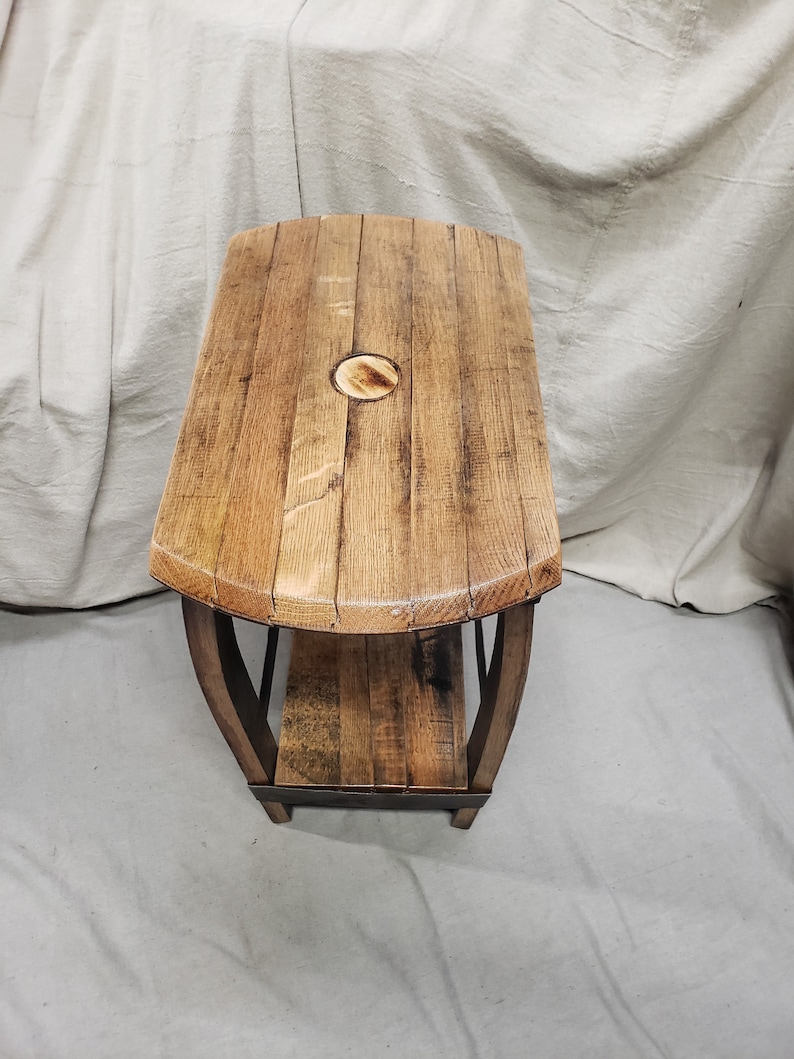 Pu&ograve; includere: Un tavolino in legno fatto a mano con doghe di botte riciclate. Il tavolo presenta un piano rettangolare con bordi arrotondati e un ripiano inferiore. Il legno ha un aspetto naturale e invecchiato con venature visibili e un colore marrone caldo. Il tavolo &egrave; sostenuto da gambe in legno curve.