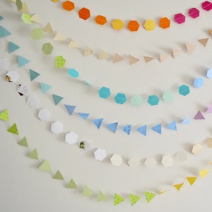 May include: A rainbow garland made of paper triangles and hexagons. The garland is made of different colors, including green, yellow, orange, pink, purple, blue, and light blue.