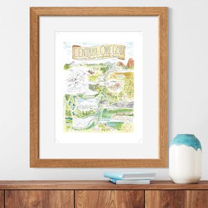 K&ouml;nnte beinhalten: Eine Aquarell-Illustration einer Karte von Central Oregon mit dem Text "Central Oregon, People & Wilderness" oben. Die Karte zeigt verschiedene Sehensw&uuml;rdigkeiten und Merkmale der Region, darunter Berge, Fl&uuml;sse, Seen und W&auml;lder. Die Illustration ist in einem hellen Holzrahmen gerahmt.