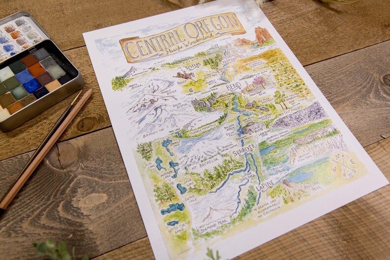 K&ouml;nnte beinhalten: Eine handgezeichnete Aquarellkarte von Central Oregon mit den Cascade Mountains, Fl&uuml;ssen, Seen und St&auml;dten. Die Karte tr&auml;gt den Titel "Central Oregon, Pacific Wonderland".