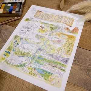 K&ouml;nnte beinhalten: Eine handgezeichnete Aquarellkarte von Central Oregon mit den Cascade Mountains, Fl&uuml;ssen, Seen und St&auml;dten. Die Karte tr&auml;gt den Titel "Central Oregon, A Piece of Wonderland".