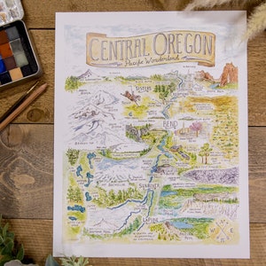 K&ouml;nnte beinhalten: Eine Aquarell-Illustration einer Karte von Central Oregon, einem Pazifischen Wunderland. Die Karte zeigt die Lage verschiedener St&auml;dte, Fl&uuml;sse, Seen und Berge in der Region. Die Karte ist von einem braunen Rahmen umgeben und enth&auml;lt eine Kompassrose unten rechts.
