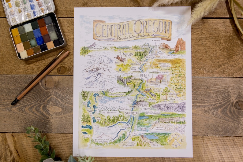 K&ouml;nnte beinhalten: Eine Aquarell-Illustration einer Karte von Central Oregon, einem Pazifischen Wunderland. Die Karte zeigt die Lage verschiedener St&auml;dte, Fl&uuml;sse, Seen und Berge in der Region. Die Karte ist von einem braunen Rahmen umgeben und enth&auml;lt eine Kompassrose unten rechts.