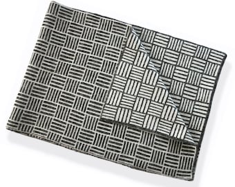 May include: A folded blanket with a black and white geometric pattern. The design consists of a repeating grid of black lines on a white background. The blanket is made of a soft material and is folded over, showing the pattern on both sides.