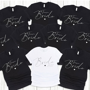 May include: Nine black t-shirts with white text that says "Team Bride" and a small heart. One white t-shirt with black text that says "Bride 2022" and a small heart.