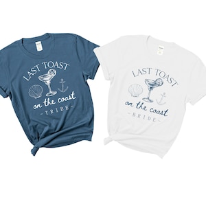 May include: Two t-shirts with a blue and white design. The text on the shirts reads "Last Toast on the Coast" with the words "Bride" and "Tribe" underneath.