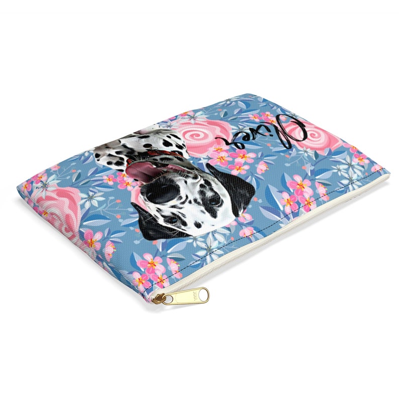 May include: A blue zippered pouch with a floral pattern featuring pink roses and white flowers. A Dalmatian dog with black spots is featured in the centre of the pouch with the name "Oliver" written in cursive above the dog.