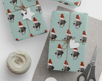 Op de afbeelding: Cadeaupapier met een herhalend patroon van een hond met een kerstmuts op een lichtblauwe achtergrond. De ingepakte cadeaus zijn vastgebonden met touw en versierd met stervormige en hartvormige labels. Een bol touw en een schaar zijn ook aanwezig.