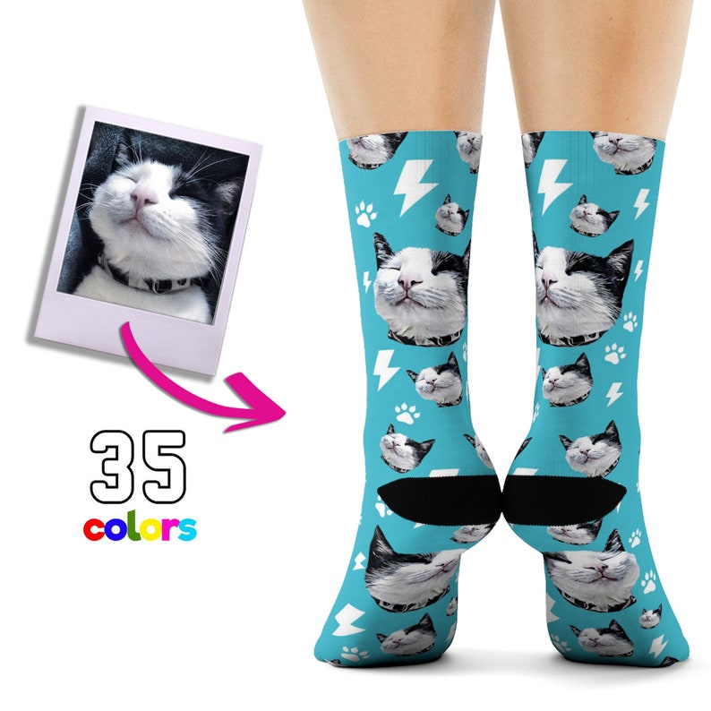 Puede incluir: Un par de calcetines azules con un patr&oacute;n de rayos blancos y huellas de patas. Los calcetines presentan una imagen repetida de un gato blanco y negro con una expresi&oacute;n feliz. El texto "35 colores" es visible debajo de la imagen.