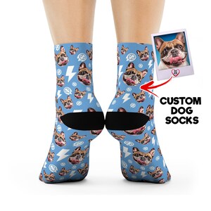 May include: Light blue custom dog socks featuring a repeating pattern of a French Bulldog's face, lightning bolts, and speech bubbles. The socks have black heels and toes. A polaroid-style image of the dog is shown with the text "CUSTOM DOG SOCKS".