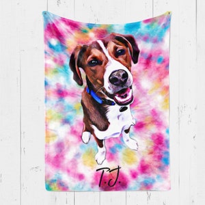 May include: A colorful tie-dye blanket featuring a portrait of a dog. The dog has brown and white fur, a blue collar, and is smiling. The blanket has a vibrant pink, blue, and yellow background. The initials "T.J." are written in black.