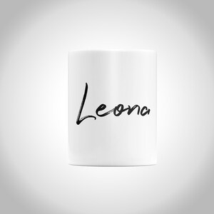 K&ouml;nnte beinhalten: Wei&szlig;e Keramiktasse mit dem Namen "Leona" in schwarzer Schrift.