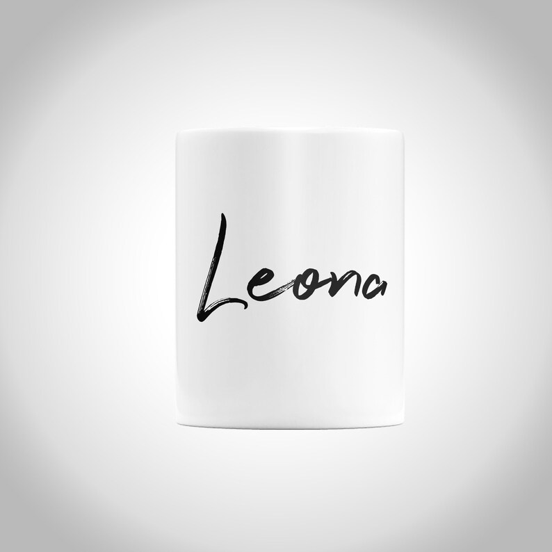 K&ouml;nnte beinhalten: Wei&szlig;e Keramiktasse mit dem Namen "Leona" in schwarzer Schrift.