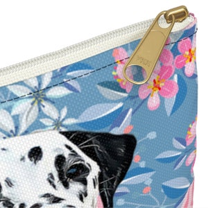 May include: A blue and white zippered pouch with a floral pattern and a Dalmatian dog face. The zipper has a gold YKK pull.