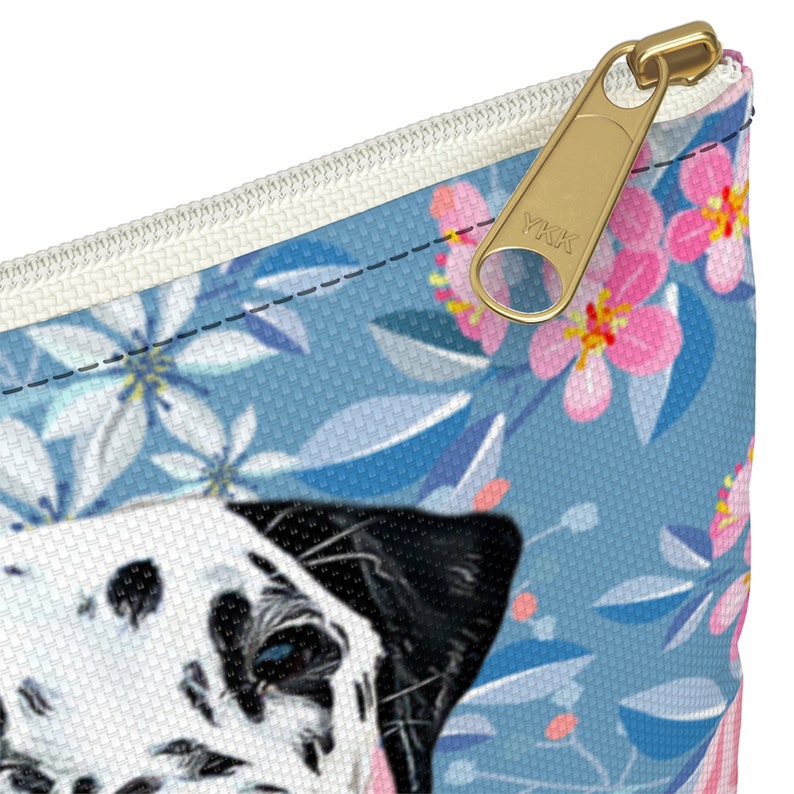 May include: A blue and white zippered pouch with a floral pattern and a Dalmatian dog face. The zipper has a gold YKK pull.