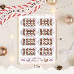 May include: A set of 8 gingerbread tray stickers featuring a gingerbread man design. Each sticker measures 8.9 cm by 11.7 cm. The stickers are printed on white paper with a pink ribbon design. The stickers are from Bubble Bear Company.