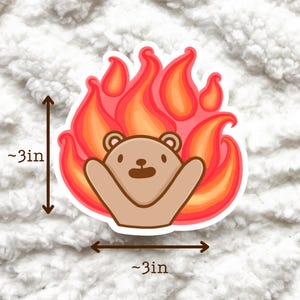 Op de afbeelding: Een gestanste sticker met een cartoonbeer in vlammen. De beer is lichtbruin met een lachend gezicht en uitgestrekte armen. De vlammen zijn rood, oranje en geel. De sticker is ongeveer 7,6 cm hoog en breed.
