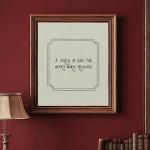 Puede incluir: Una impresión enmarcada con el texto "A thrill of hope the weary world rejoices" en un marco decorativo. La impresión se muestra en una pared roja sobre una estantería de madera con libros y una lámpara.