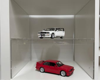 May include: A white display shelf with two model cars. The top shelf holds a white car with an open door. The bottom shelf displays a red car. Both cars have detailed features and are miniature replicas.