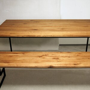 May include: A wooden dining table and bench set. The table and bench have a natural wood finish and black metal legs. The table is rectangular, and the bench is a smaller version of the table. The set is suitable for a dining room or kitchen.