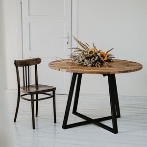 Peut inclure: Une table ronde en bois avec une base en métal noir et une chaise en bois. La table est ornée d'un bouquet de fleurs séchées et de tournesols. La chaise est en bois foncé.
