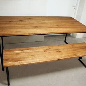 May include: A rectangular wooden dining table and matching bench. The tabletop and bench seat are made of light brown wood. The table and bench have black metal legs. The table is approximately 72 inches long.