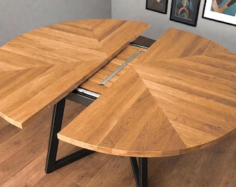 May include: A round, extendable wooden table with a light brown finish. The tabletop is divided into two semi-circular sections with a chevron pattern. The table has a black metal base and is partially extended, revealing the extension mechanism.