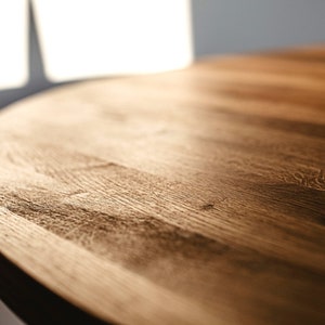 May include: Close-up of a round wooden table top with a natural wood grain finish. The surface is smooth and polished, with a warm brown color.