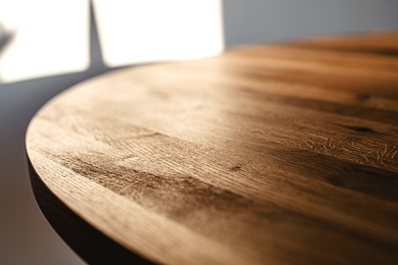 May include: Close-up of a round wooden table top with a natural wood grain finish. The surface is smooth and polished, with a warm brown color.