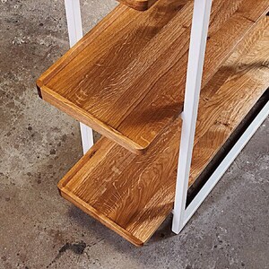 Puede incluir: Estanter&iacute;a de metal blanco con tres estantes de madera. Los estantes son de madera natural con un acabado marr&oacute;n claro.