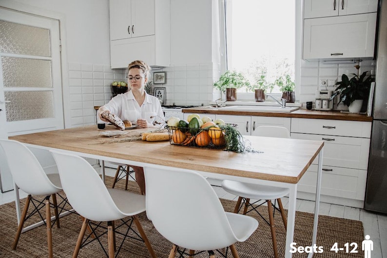 May include: A white kitchen table with a wooden top and metal legs. The table is set with a bowl of fruit, a loaf of bread, and a plate. There are four white chairs around the table. The text "Seats 4-12" is visible in the lower right corner of the image.
