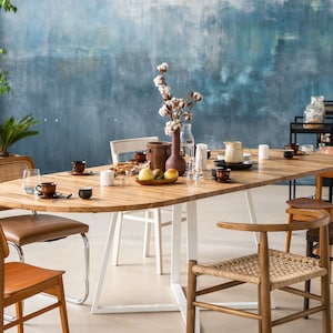 Könnte beinhalten: Ein ovaler Esstisch aus hellem Holz mit weißen Metallbeinen, umgeben von sechs Stühlen. Der Tisch ist mit Geschirr, Tassen und einer Schale Obst gedeckt. Eine Vase mit Baumwollblumen steht in der Mitte des Tisches.