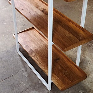 Puede incluir: Una estanter&iacute;a de metal blanco con tres estantes de madera. Los estantes son de madera natural con un acabado marr&oacute;n claro. El marco de metal est&aacute; pintado de blanco.