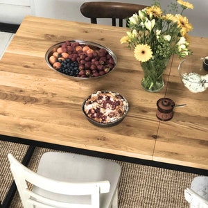 May include: A wooden table set for a meal with a variety of food items, including a fruit salad, a pie, a bowl of salad, and a plate of avocado and red radishes. There is also a vase of flowers and a small ceramic jar with a spoon.