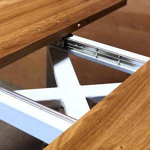 K&ouml;nnte beinhalten: Nahaufnahme eines Holztisches mit einem wei&szlig;en Metall-Ausziehmechanismus. Die Tischplatte ist aus Holz und hat eine nat&uuml;rliche Oberfl&auml;che. Der Ausziehmechanismus ist aus Metall und hat eine silberne Oberfl&auml;che.