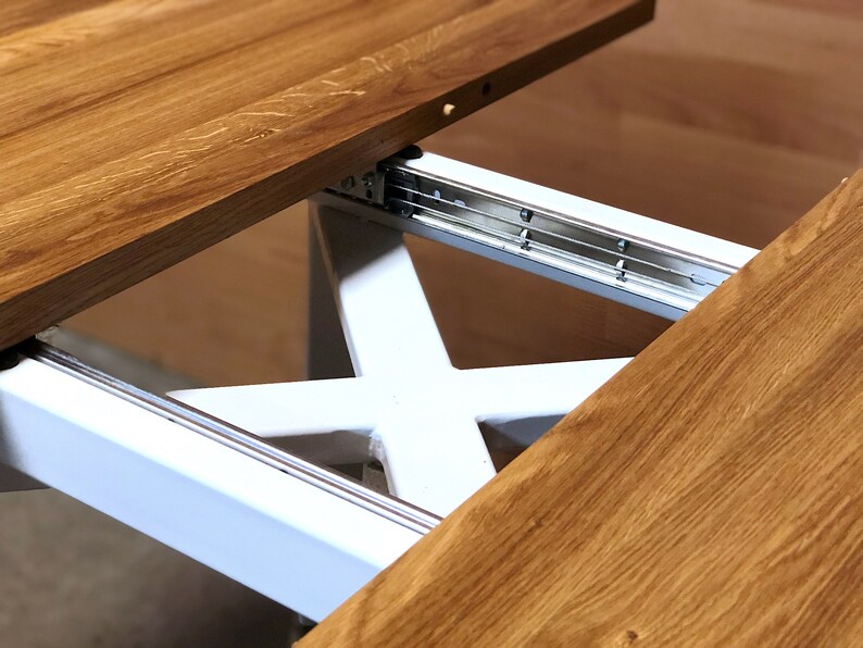 K&ouml;nnte beinhalten: Nahaufnahme eines Holztisches mit einem wei&szlig;en Metall-Ausziehmechanismus. Die Tischplatte ist aus Holz und hat eine nat&uuml;rliche Oberfl&auml;che. Der Ausziehmechanismus ist aus Metall und hat eine silberne Oberfl&auml;che.