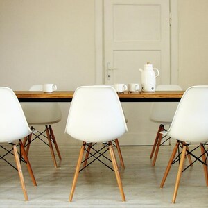 May include: A dining room set featuring a rectangular wooden table with a black metal frame. White plastic chairs with wooden legs and black metal supports surround the table. A white teapot, cups, and a white door are in the background.