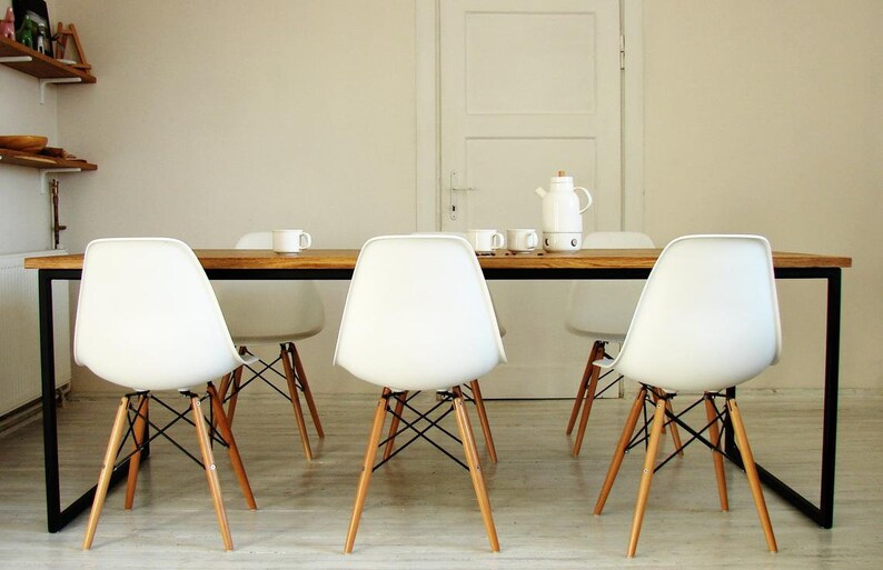 May include: A dining room set featuring a rectangular wooden table with a black metal frame. White plastic chairs with wooden legs and black metal supports surround the table. A white teapot, cups, and a white door are in the background.