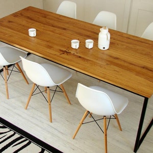 May include: A rectangular wooden dining table with a natural finish and black metal legs. Six white chairs with wooden legs and a white kettle and cups are arranged around the table. A black and white zebra-striped rug is in the foreground.