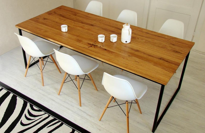 May include: A rectangular wooden dining table with a natural finish and black metal legs. Six white chairs with wooden legs and a white kettle and cups are arranged around the table. A black and white zebra-striped rug is in the foreground.